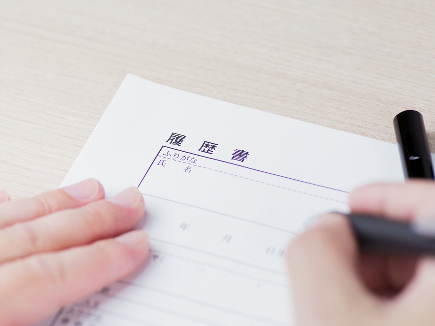 ペンを持ち、履歴書を書いている手の写真